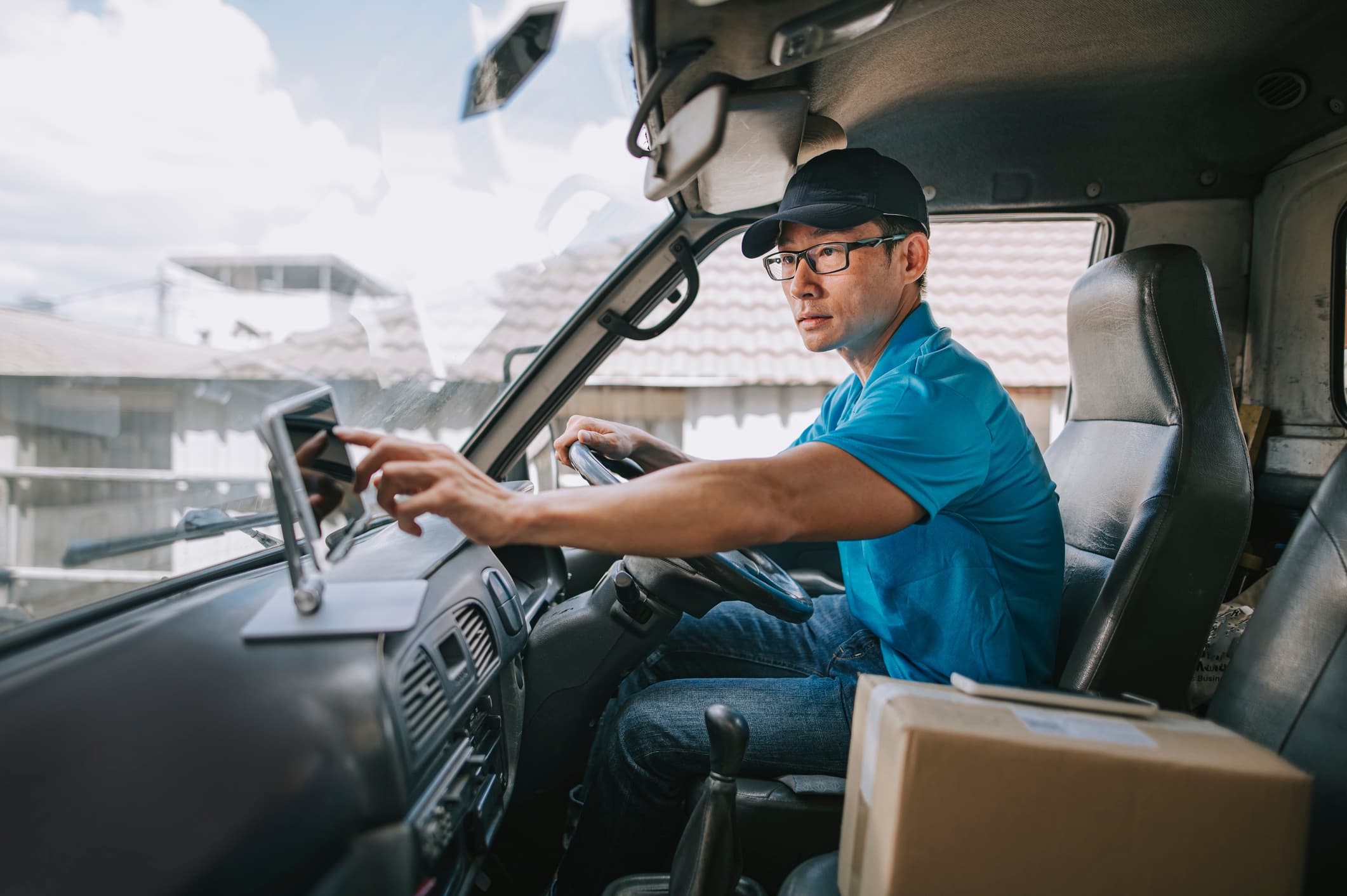 A mature Chinese male delivery driver in a delivery van, checking delivery information on a mobile app for a startups supply chain management system.