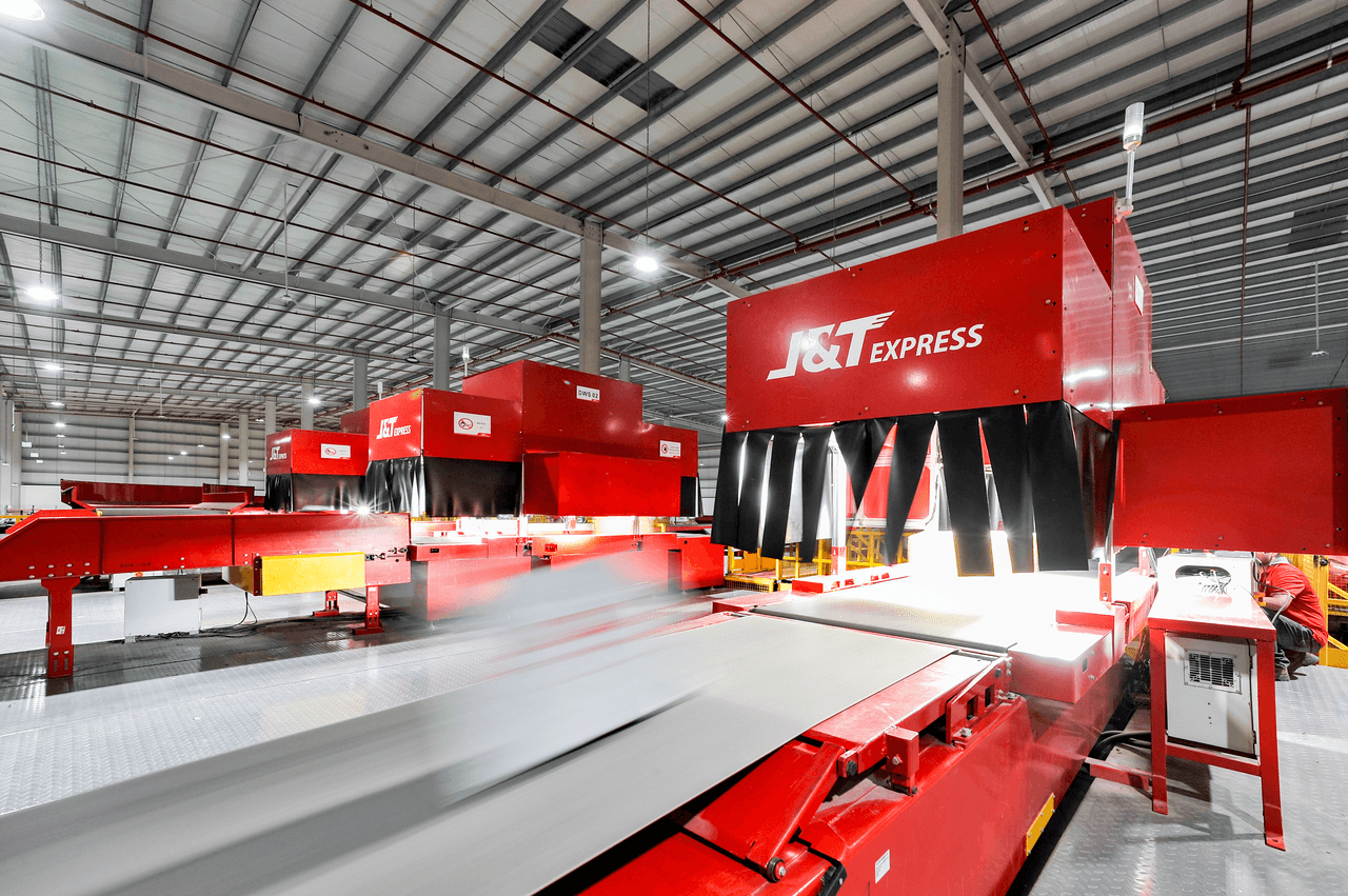 Automated J&T Express sorting facility, showcasing red conveyor belts efficiently moving parcels for FMCG logistics, highlighting digitalized operations in a large, well-lit warehouse.